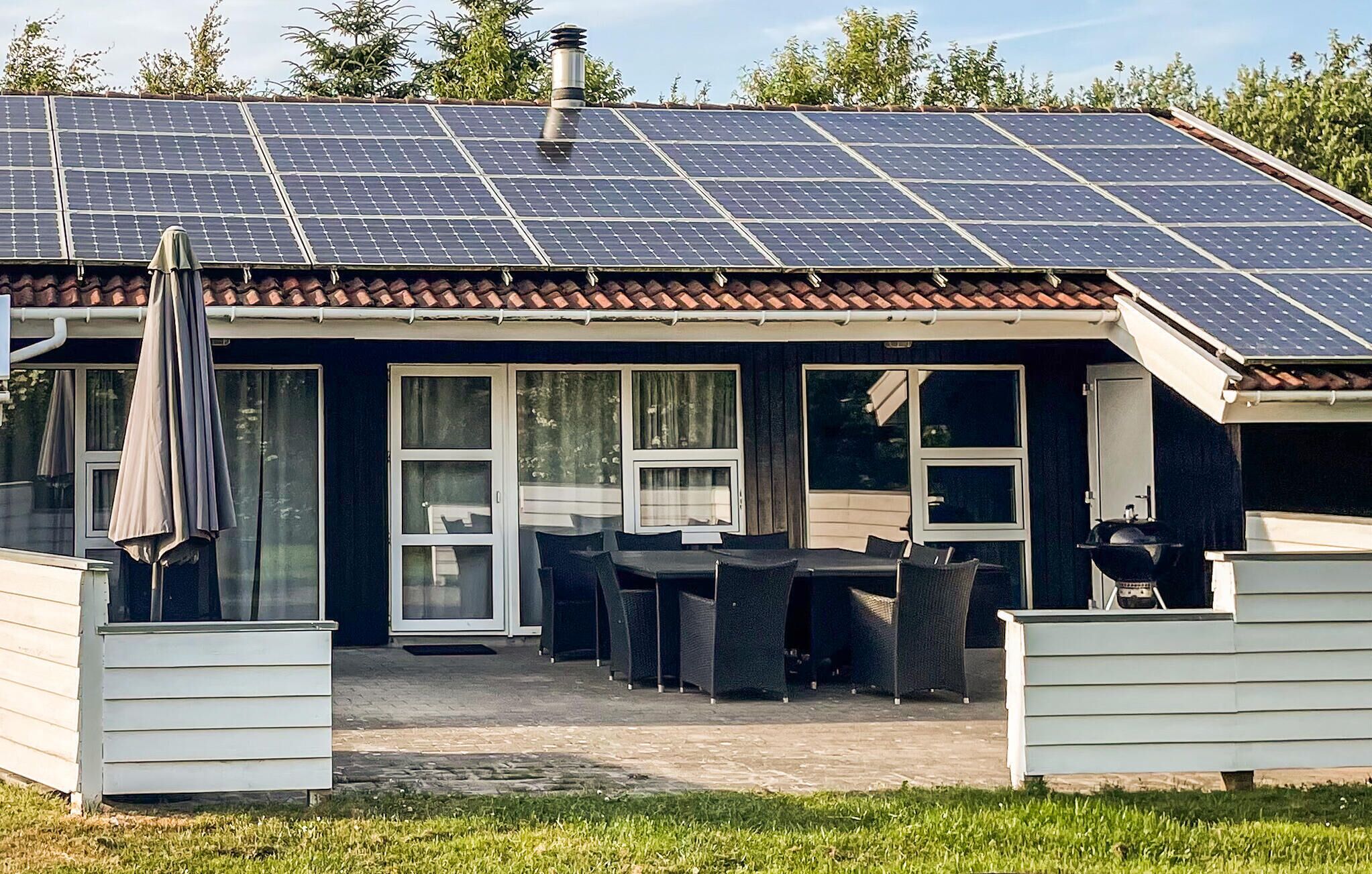 Une maison dotée d’un toit recouvert de panneaux solaires, d’un patio avec des meubles d’extérieur et d’un espace abrité équipé d’un barbecue.