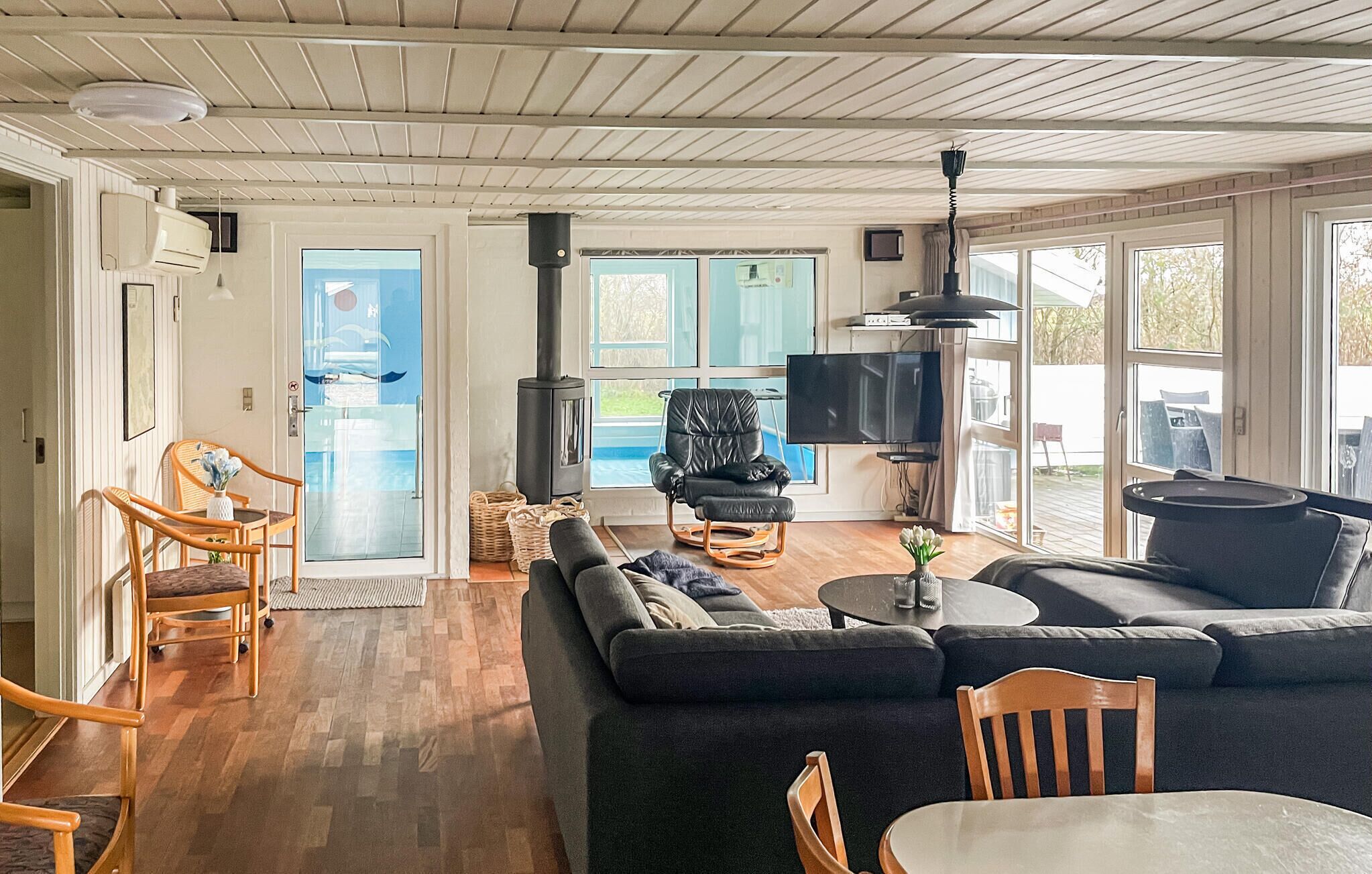 Ein Wohnzimmer mit einer Couch, Sesseln, einem Fernseher, einem Kamin und Blick ins Freie.