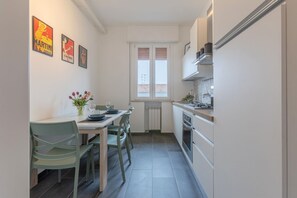 Una cocina estrecha con zona de comedor, armarios blancos y una ventana con persianas.