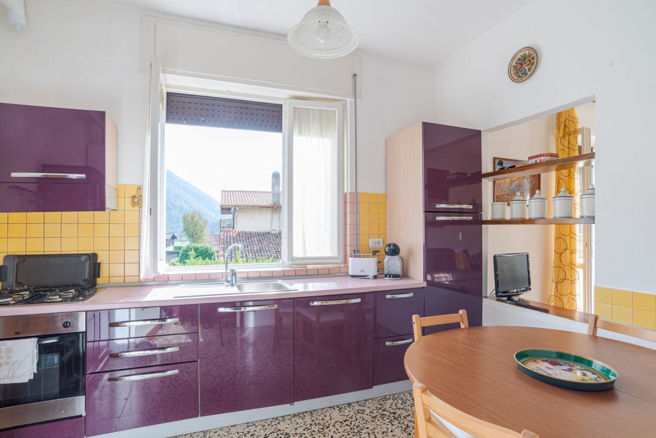 A kitchen with purple cabinets, a wooden dining table, and a window with a view of a house and mountains.