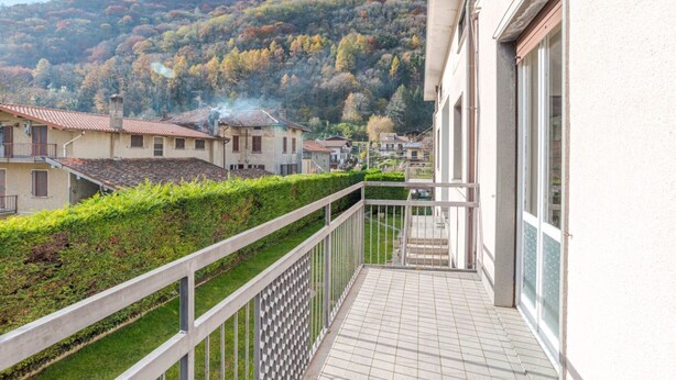 Ein Balkon mit Blick auf eine Hügelkuppe, ein Gebäude mit Ziegeldach und ein Hecke.