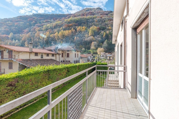 Un balcon donnant sur une colline, un bâtiment avec un toit en tuiles et une haie.