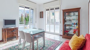 Ein Essbereich mit Tisch und Stühlen, einem Fernseher auf einer Holzkommode, einem roten Sofa und einer Glasvitrine mit Geschirr.