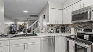 Una cucina moderna con mobili bianchi, forno in acciaio inossidabile, microonde e schienale piastrellato.