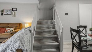 Una scala conduce a un secondo piano, con un'area pranzo con tavolo e sedie e un divano con una coperta.