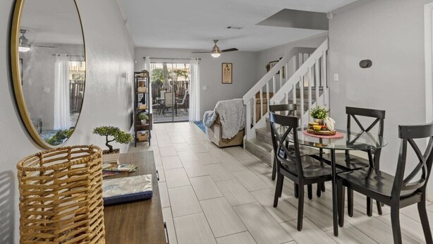 Un'ampia sala con zona pranzo, caratterizzata da un tavolo in vetro e sedie scure, un grande specchio e una scala che conduce a un altro piano.