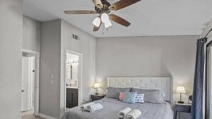 Una camera da letto con un letto, comodini, una ventola a soffitto e una finestra con tende.
