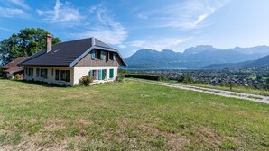 Ein Haus mit schrägem Dach, einem Schornstein und Blick auf ein Tal und Berge.