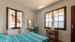Ein Schlafzimmer mit Bett, Schreibtisch, Stuhl, einem Fenster mit Vorhängen, einem Waschbecken und einem Spiegel.