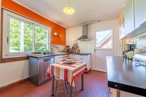 Una cocina con mesa de comedor, lavavajillas, estufa y ventana con vista a árboles.
