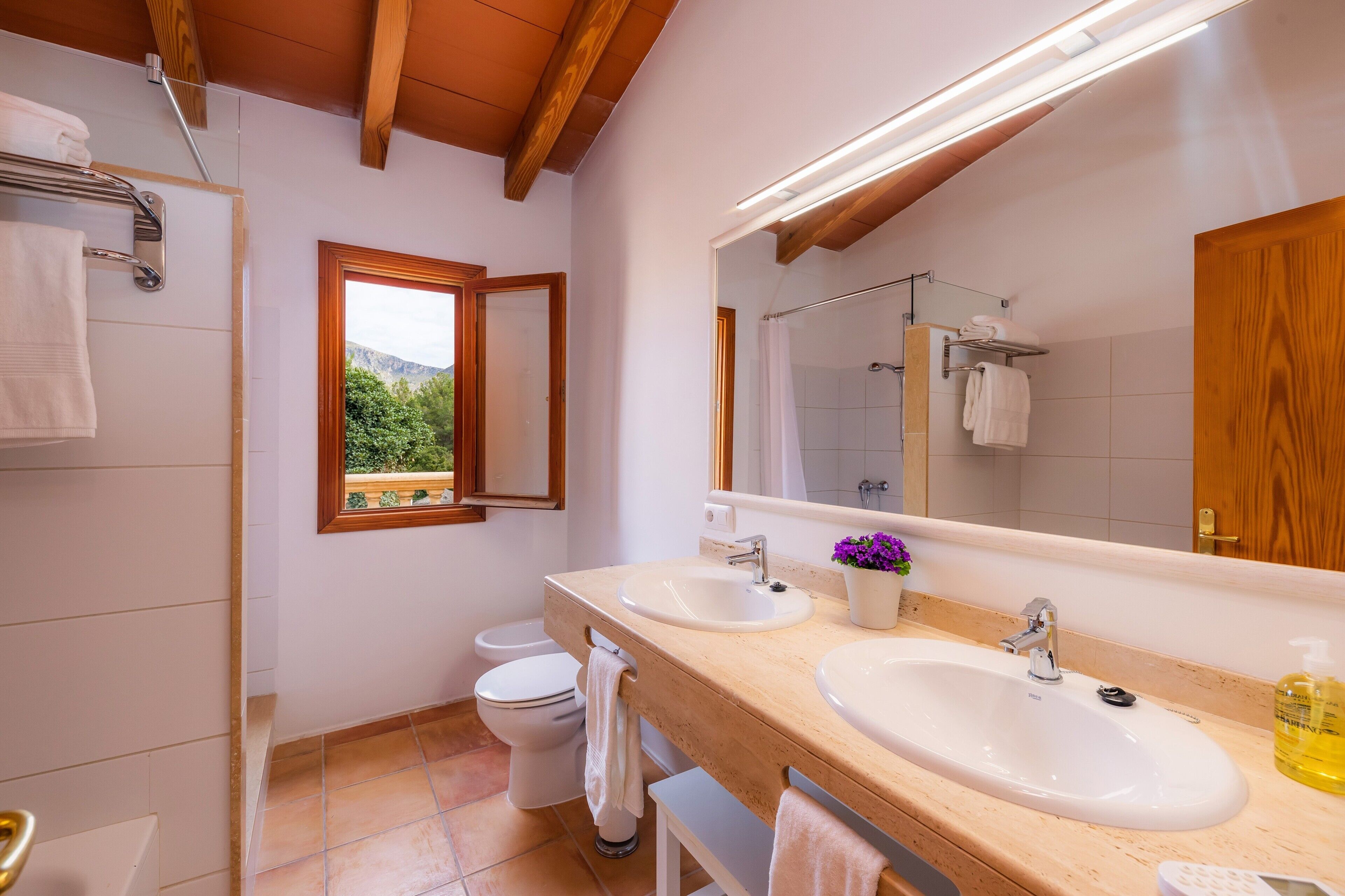 Ein Badezimmer mit zwei Waschbecken, einer Toilette, einer Dusche und einem Fenster mit Blick auf Grünflächen.
