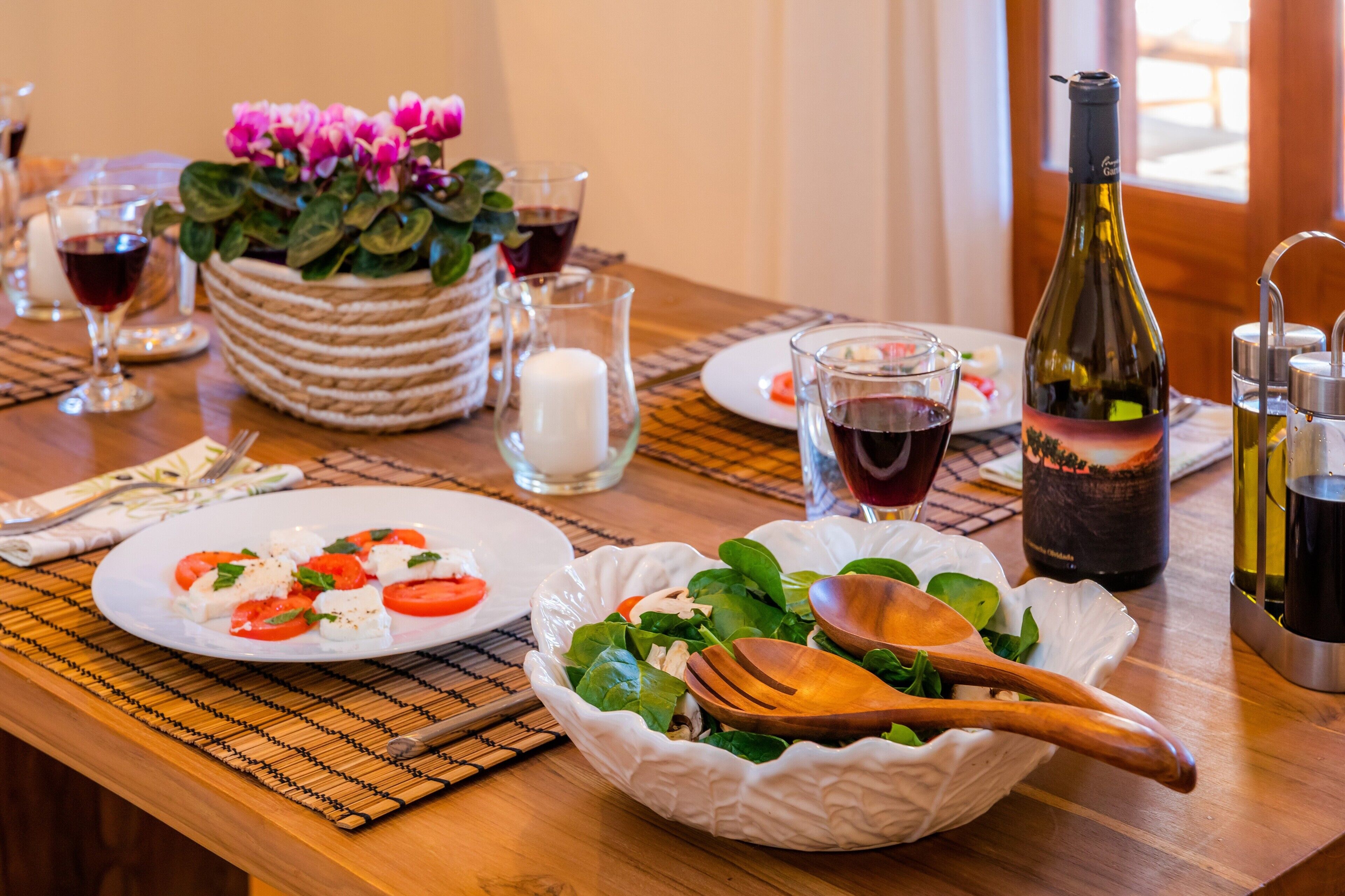 A dining table with plates of food, a bottle of wine, and a bowl of salad.