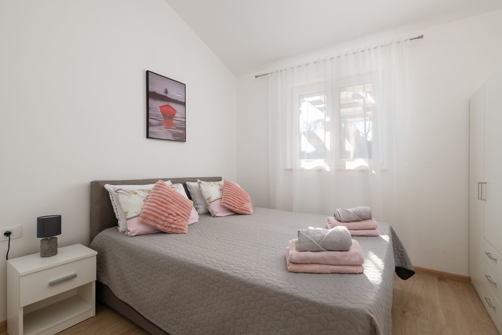 A bedroom with a bed, pillows, a nightstand, a lamp, and a window with curtains.