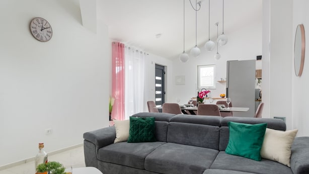 Una sala de estar moderna con un sofá gris, una mesa de centro blanca y una pequeña planta en maceta. Al fondo, se distingue un área de comedor con una mesa y sillas.