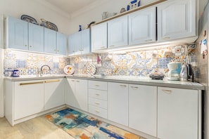 Een keuken met lichtblauwe kastjes, een kleurrijke tegelachtergrond en een vloerkleed met dessin.