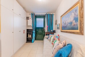 Une pièce avec une porte verte, un canapé orné de coussins à motifs floraux, un tableau encadré et une étagère remplie de bouteilles.
