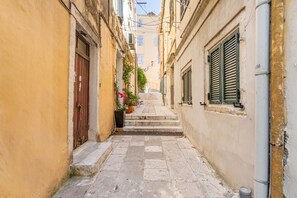 A narrow street with stone pavement, buildings on either side, and a staircase leading to a higher level.