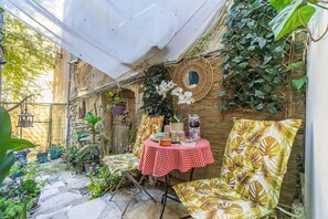 A covered outdoor seating area with a table, chairs, and potted plants.