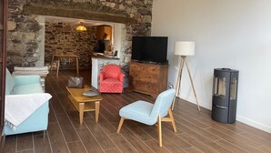 Un salon avec des murs en pierre, une télévision, une lampe, un fauteuil, un canapé et une table.
