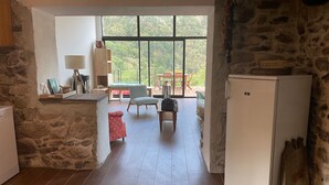Une pièce avec un mur en pierre, un réfrigérateur blanc, une table en bois et une fenêtre donnant sur un paysage verdoyant.