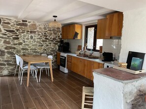A kitchen with stone walls, wooden cabinets, a dining table with chairs, a coffee machine, and a sink. - 'Maison Gaia' with Private Terrace, Wi-Fi, and Air Conditioning (VALDEBLORE)