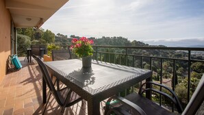 Un balcón con mesa y sillas, una planta en maceta y vistas a un paisaje montañoso.