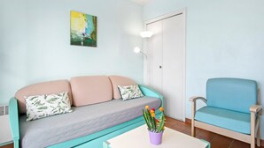 Una habitación con un sofá azul verdoso, un sillón azul, una puerta blanca y un cuadro en la pared.