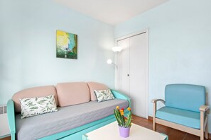 A room with a teal sofa, a blue chair, a white door, and a painting on the wall.