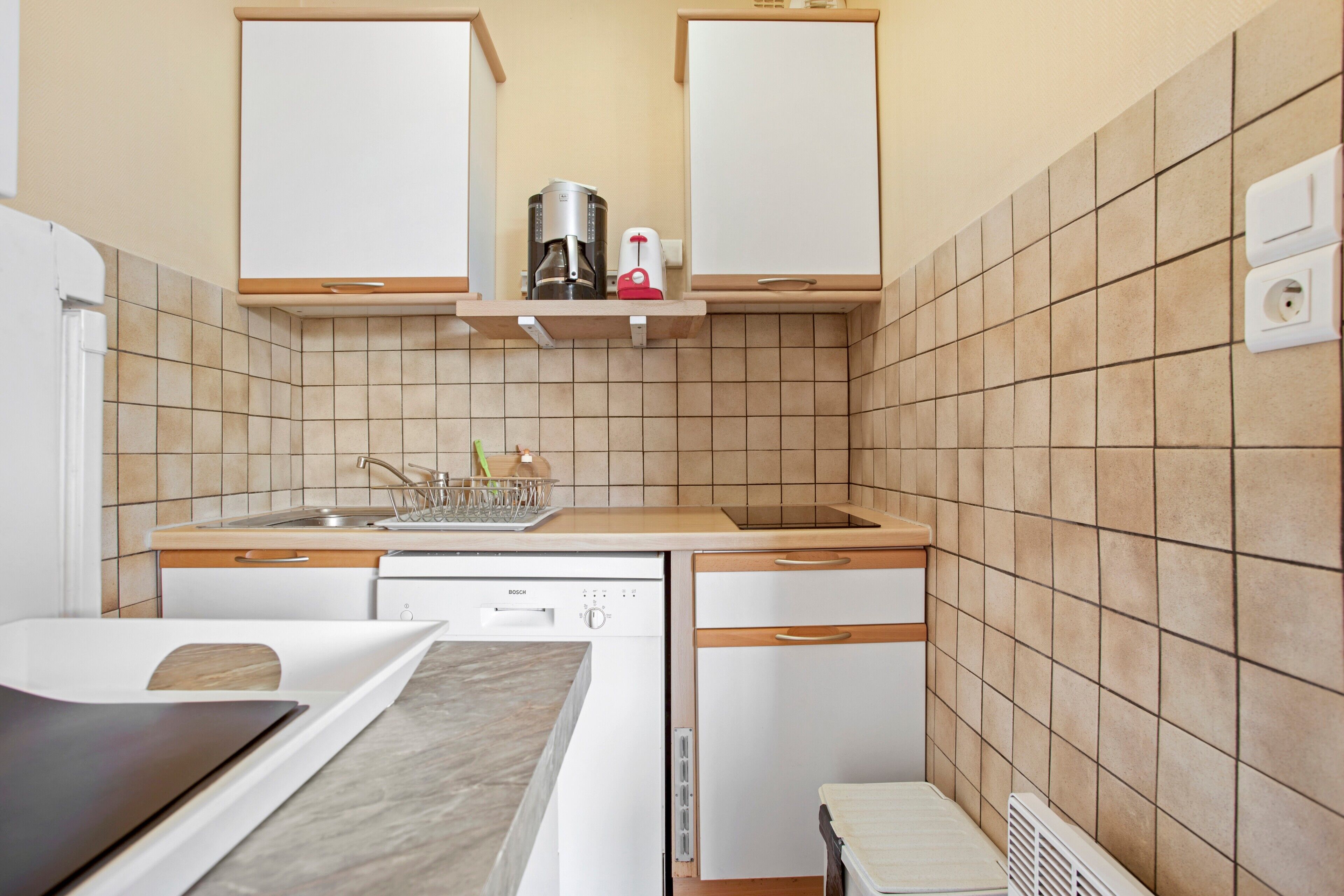 Een compacte keuken met een Bosch vaatwasser, een koffiezetapparaat en een magnetron op een plank.