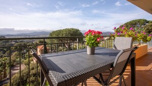 Un balcon avec une table et des chaises, un pot de fleurs, et une vue sur le paysage.