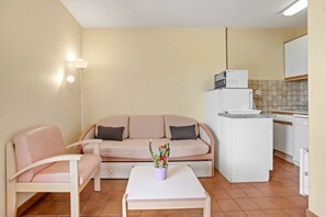 Un espace de vie compact comprenant un canapé, une petite table, un coin cuisine et une plante en pot.