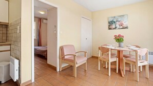 Une pièce comprenant un lit, une table avec des chaises, un radiateur, une porte et un tableau accroché au mur.