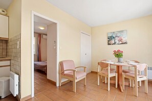 Ein Zimmer mit einem Bett, einem Tisch mit Stühlen, einem Heizkörper, einer Tür und einem Bild an der Wand.