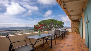 A balcony with a table and chairs, a vase of flowers, and a view of the landscape.