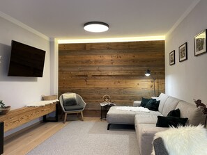Een moderne woonkamer met een houten accentmuur, een flatscreen televisie, een bank, een fauteuil en een salontafel.
