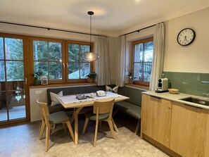 Een gezellige keuken met een houten tafel, twee stoelen, een bank en een raam met gordijnen.