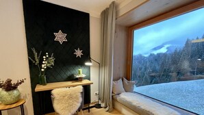 Ett mysigt rum med ett skrivbord i trä, en mjuk fåtölj, ett fönster med utsikt över ett snötäckt berg och en svart vägg dekorerad med stjärnor.