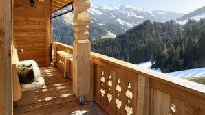 Un balcon en bois offrant une vue sur des montagnes enneigées et une vallée boisée.