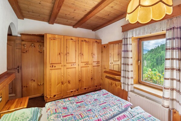 Una habitación de madera con cama, armario y ventana con vistas a la vegetación.