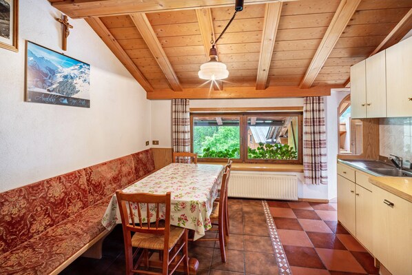A dining area with a wooden bench, a table with a floral tablecloth, and a view of greenery outside.