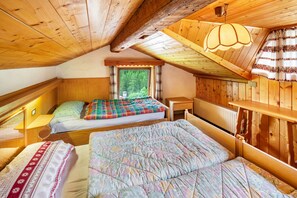 Un dormitorio acogedor en el ático, con paredes de madera, una ventana con cortinas, una cama con colcha colorida y una lámpara colgante.