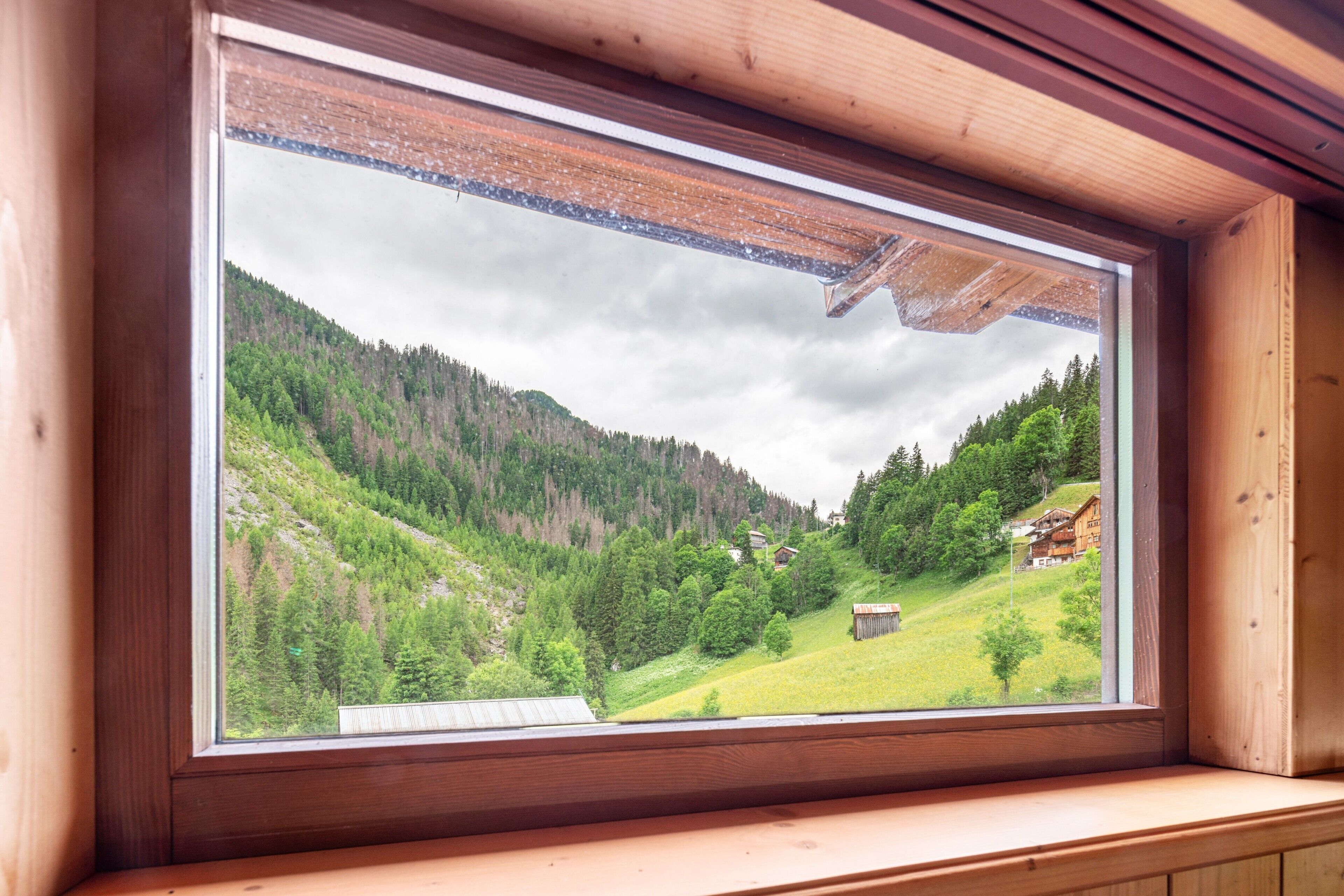 Ein Fenster mit Blick auf ein grünes Tal und eine Holzhütte.