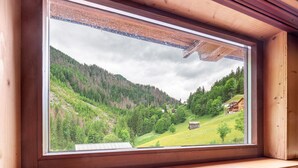 Ein Fenster mit Blick auf ein grünes Tal und eine Holzhütte.