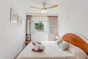 Une chambre d’hôtel avec un lit, un ventilateur de plafond, une fenêtre avec des rideaux et des tableaux encadrés accrochés au mur.