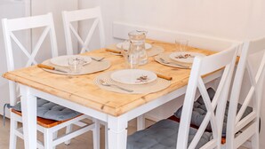 Ein Esstisch ist gedeckt mit Tellern, Besteck und einer Karaffe, umgeben von weißen Stühlen mit gepolsterten Sitzen.