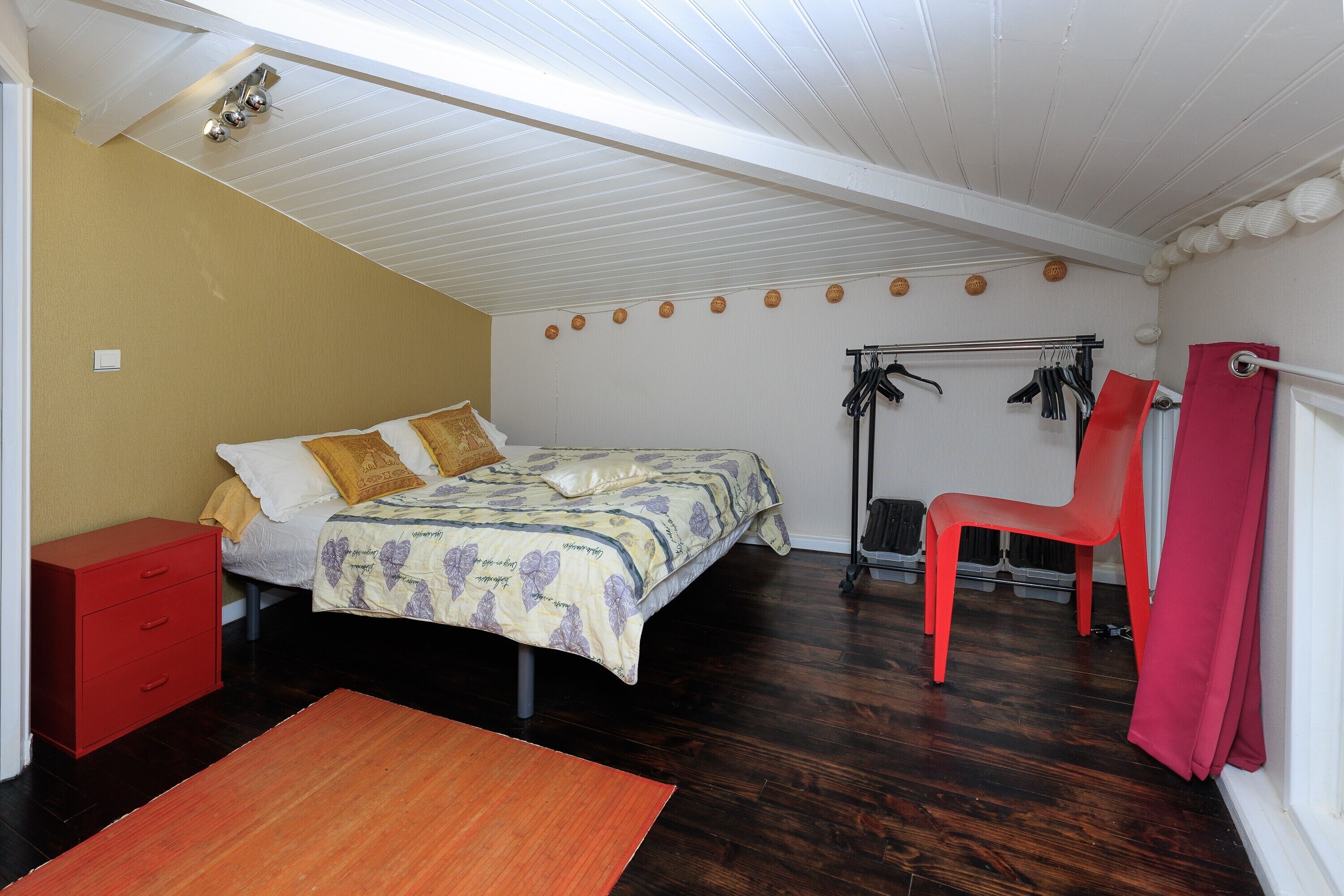 A bedroom with a bed, a red chair, a red dresser, and a wooden floor.