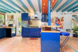 Una cocina moderna con armarios azules, una isla central y una zona de comedor con un taburete azul.