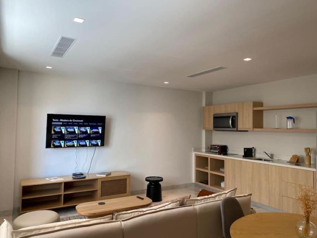 A modern living room with a flat-screen TV mounted on the wall, a wooden coffee table, and a sofa.