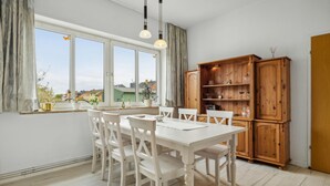A dining area with a white table and chairs, a wooden cabinet with shelves, and a window with curtains. - Lovely apartment in Malchow with WiFi (Malchow)