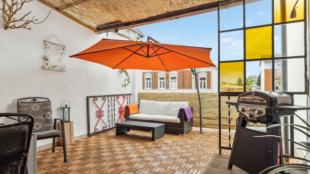 A covered outdoor seating area with a wooden floor, a grill, and a large orange umbrella. - Lovely apartment in Malchow with WiFi (Malchow)
